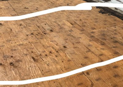 A section of a wooden roof deck with clearly visible water stains and dark spots, outlined with a thick irregular white line. The area shows signs of wear and possible water damage.