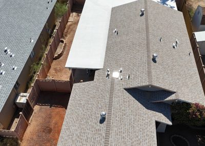 Aerial view of two neighboring houses with gray shingle roofs, a covered patio, and a small fenced backyard with a garden area and gravel paths.
