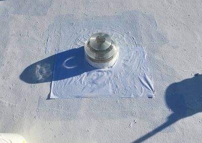 A round glass dome skylight is installed on a flat, white-painted roof with visible brush marks. The skylight casts a distinct shadow to the left in the sunlight.
