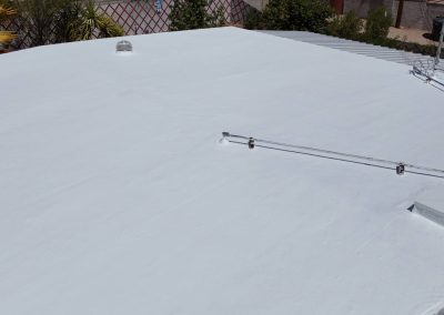 A flat white-painted roof with a few small vents and pipes, surrounded by greenery and some fencing in the background.
