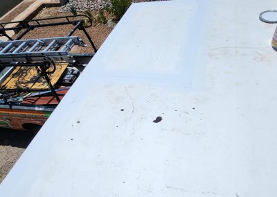 View from a rooftop showing a white, slightly dirty rooftop surface with cans placed on it; a truck with a ladder rack and some equipment is parked below next to a gravel area.
