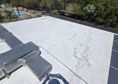 Flat white rooftop with some discoloration and minor stains, visible HVAC ductwork, surrounding trees, and a swimming pool in the background. A shadow of the person taking the photo appears in the foreground.