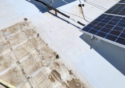 Close-up of a white rooftop with visible damage and peeling material on the left side; solar panels and electrical cables are installed on the right side.