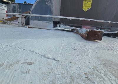 View of a white-coated flat rooftop with construction materials, including a wooden plank and a metal bar, near an HVAC unit. A yellow warning label is visible on the unit in the background.