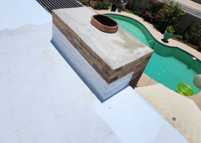 A view from a rooftop shows a brick chimney, a backyard swimming pool with inflatables, and a striped umbrella on a sunny day. Some greenery and a garden are visible around the pool area.